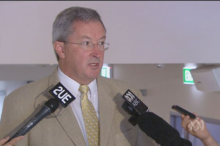 A man in a suit speaks into microphones at a press conference.