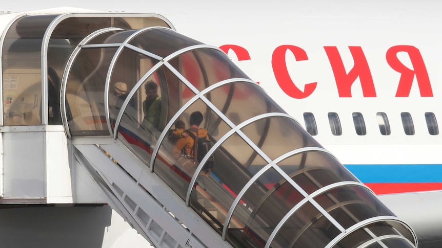 People walk up stairs to a Russian plane.