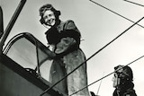 Black and white photo of a man and a woman boarding a Tiger Moth Plane wearing heavy flying clothes and goggles