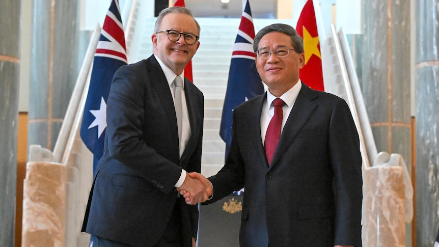 Anthony Albanese wears a dark suit, smiles, and shakes hands with Li Qiang who is in a black suit