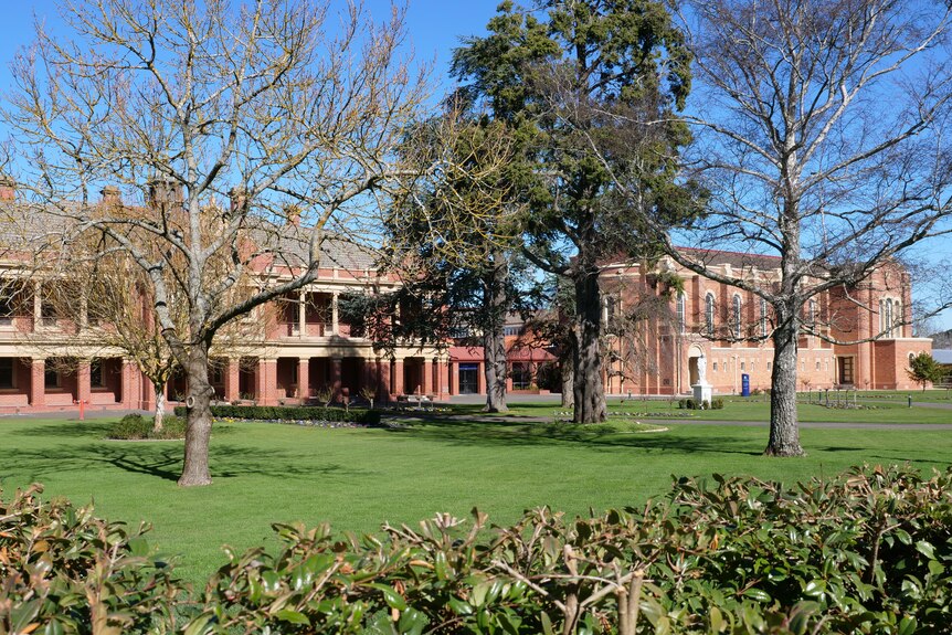 Two large old school buildings with trees and grass in front. 