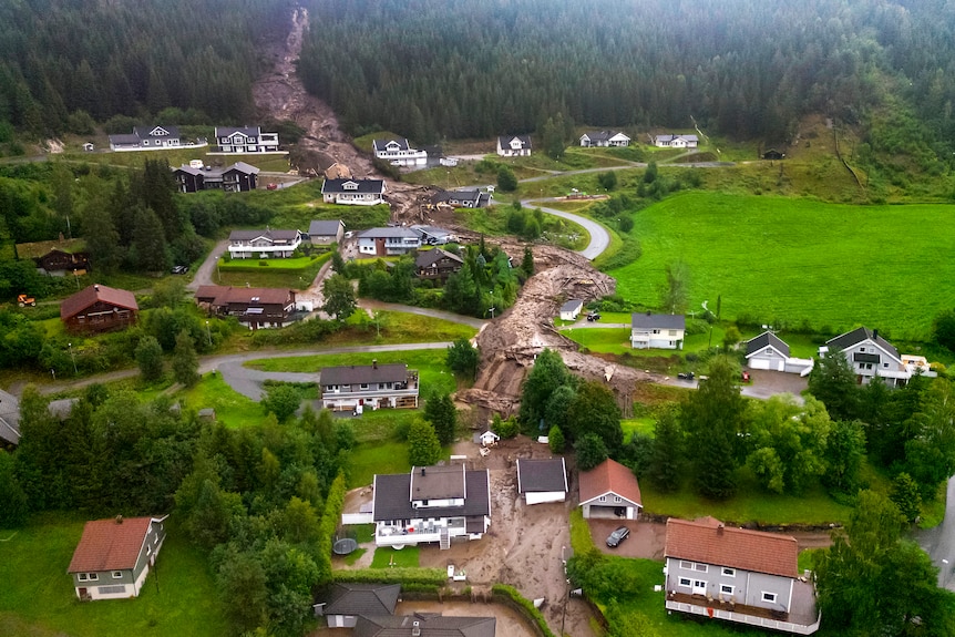 A valley of houses surrounded by green pasture and mud from a landslide