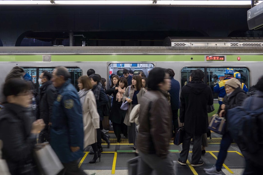 Commuters exit a train at the platform at night in Shibuya, Japan, as others walk across the platform in blurry image.