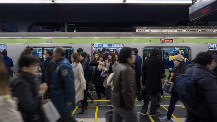 Commuters exit a train at the platform at night in Shibuya, Japan, as others walk across the platform in blurry image.