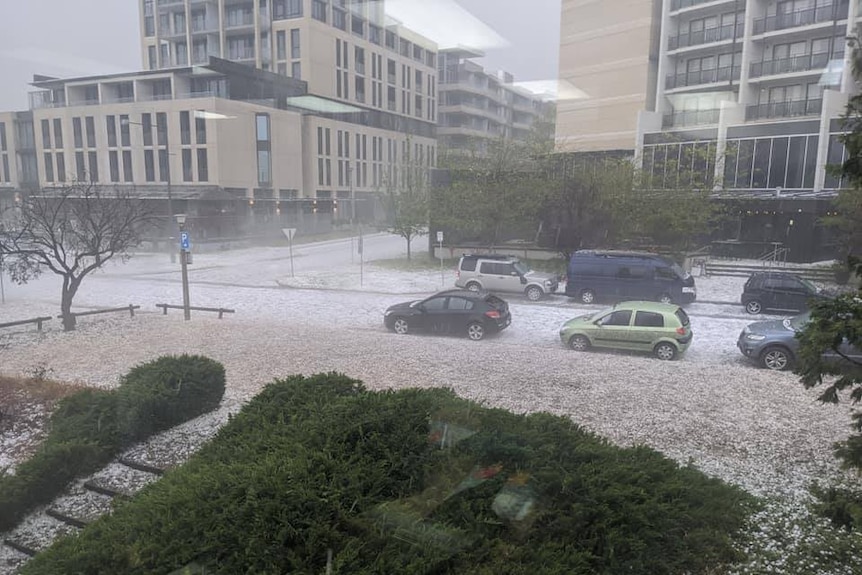 Hailstones coat a grassed area and streets at ANU, with grey skies making an ominous backdrop.