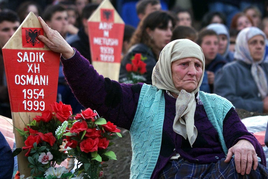 A grief stricken woman with her son's headstone in a crowd of supporters