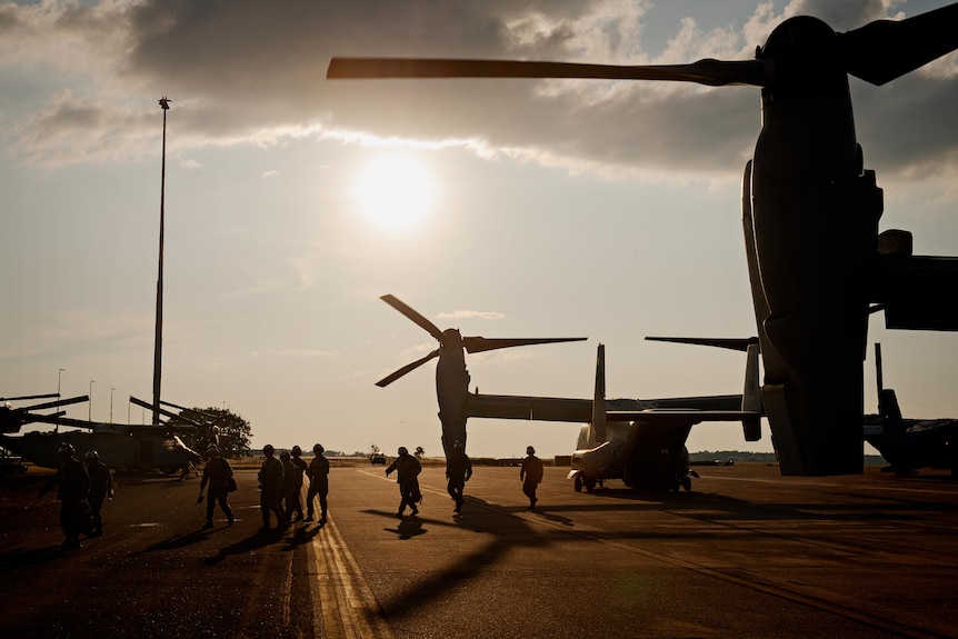 A line of soldiers walking off a military plane parked on a runway, close to sunset.