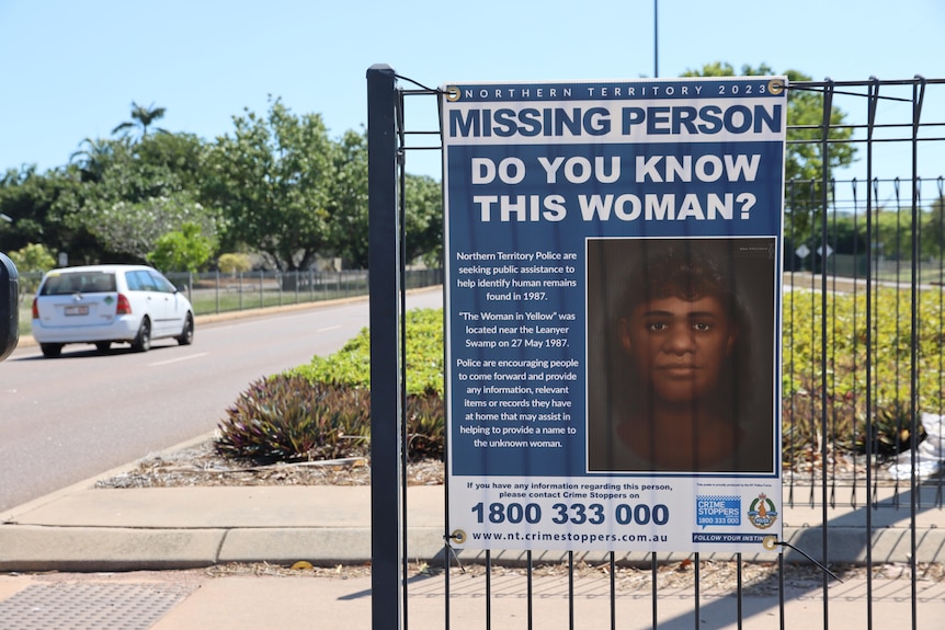 A poster attached to a fence says 'missing person, do you know this woman' and has a digitised image of a woman's face on it