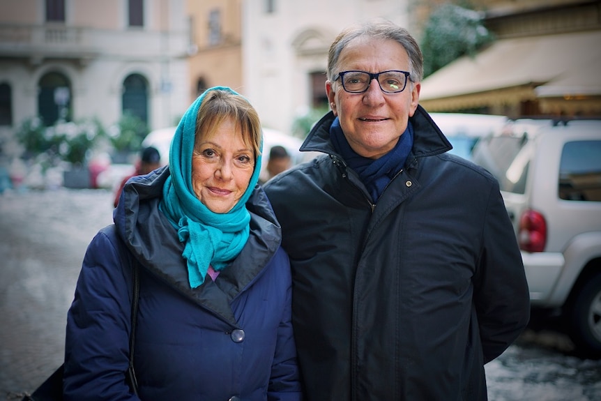 A middle-aged man and woman stand together in an Italian street.