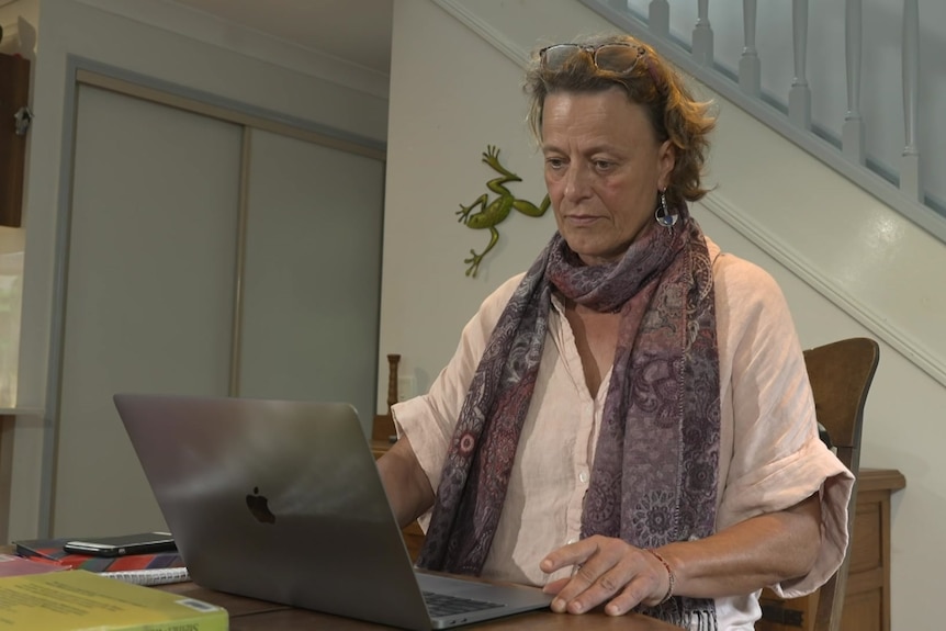 A woman with short curly hair and a purple scarf sits, looking down at a laptop.