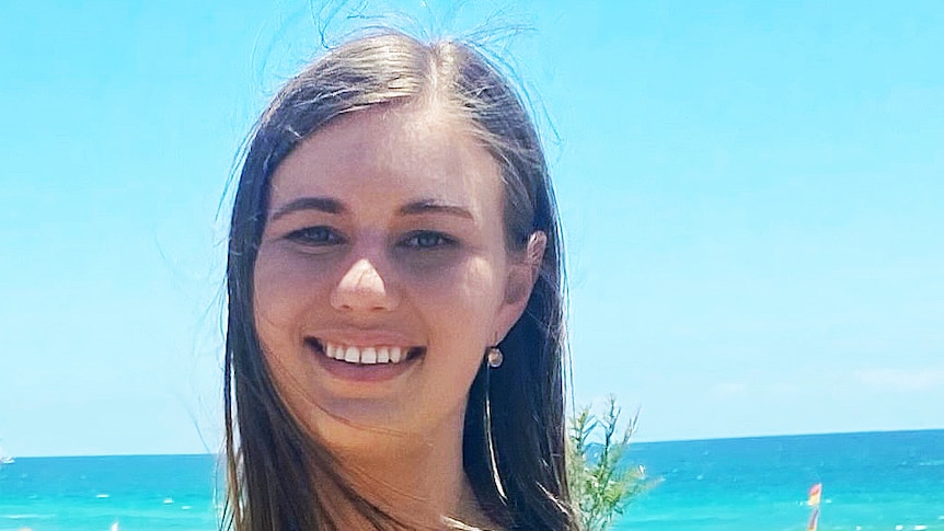 A woman smiles with a beach behind