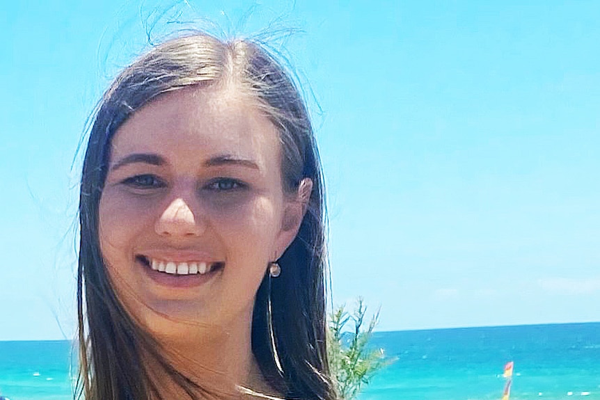 A woman smiles with a beach behind