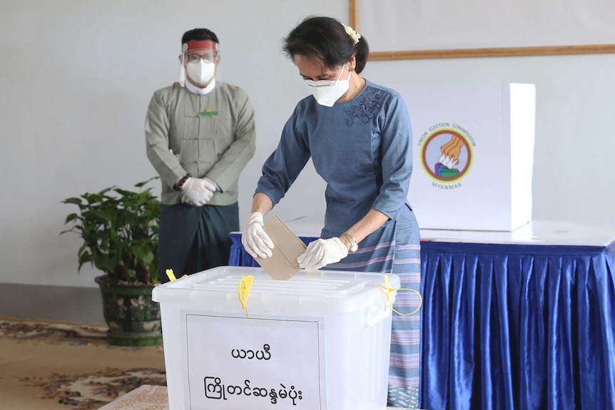 Myanmar leader Aung San Suu Kyi wears a facemask as she places a ballot in a box.