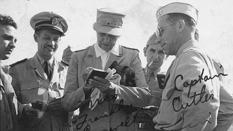 A black and white photo of soldiers with a woman signing a notebook in the middle