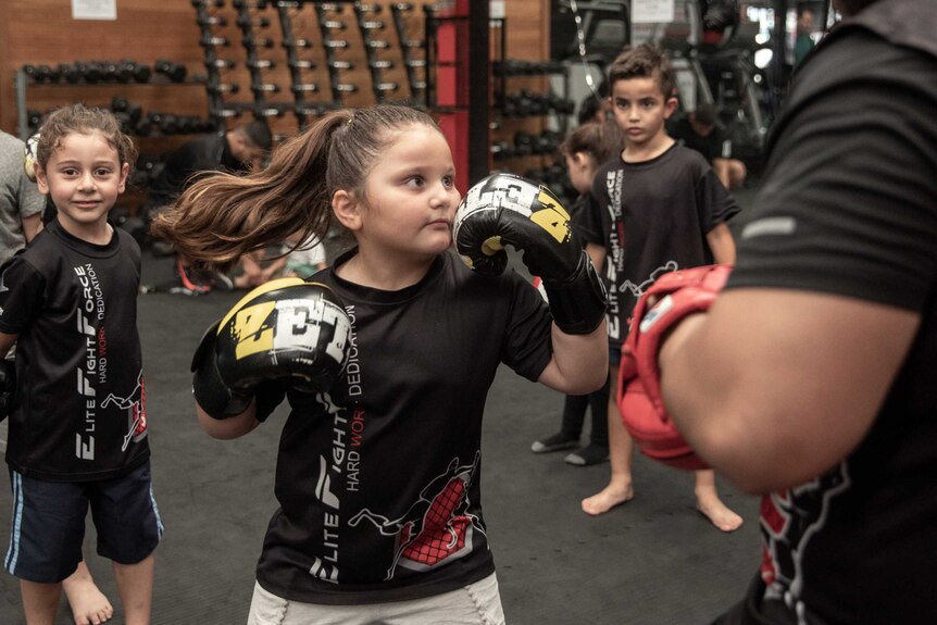 An action shot of a young girl throwing a punch at her trainer in a gym.