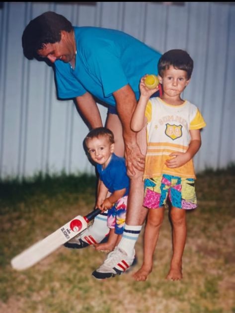 Two children holding a ball and a bat and a man crouched over behind them.