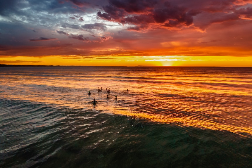 A sunrise over the ocean with a group of people in the water.