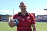 A man in a red shirt standing on a football field with a ball under his arm