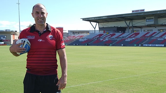 A man in a red shirt standing on a football field with a ball under his arm