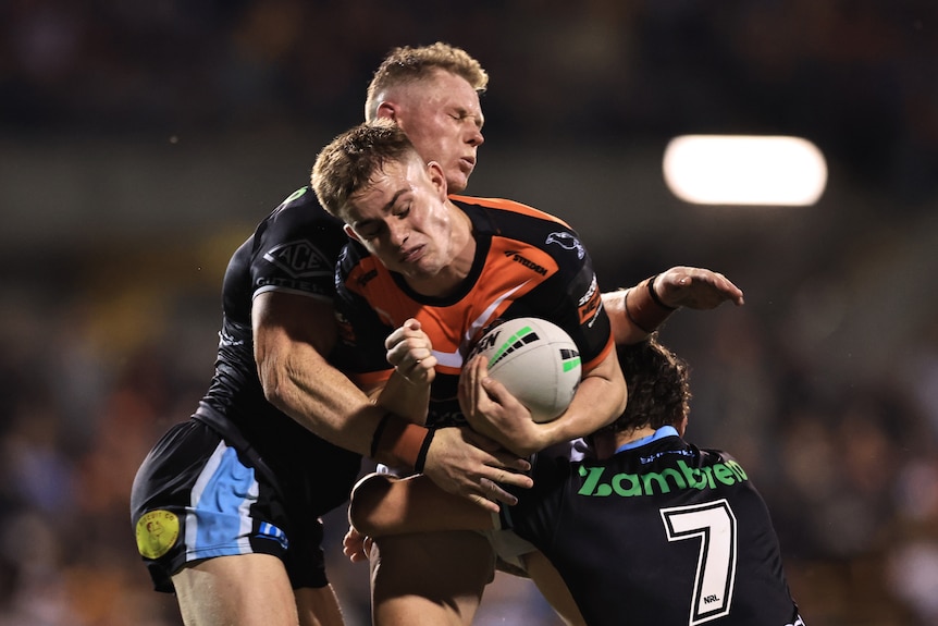 NRL player Lachlan Galvin of the Wests Tigers tackled against the Cronulla Sharks during a night match