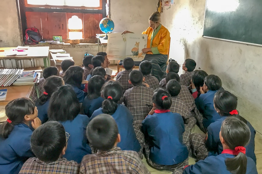 Young school students in Bhutan sit listening to an English teacher read from a picture book.