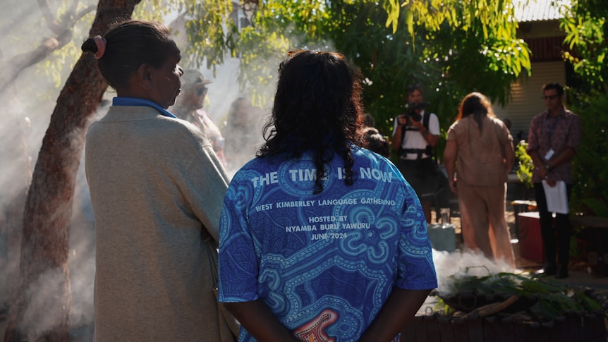 The back of two women standing in front of a smoke from a smoking ceremony