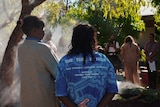 The back of two women standing in front of a smoke from a smoking ceremony