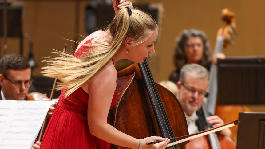 Double bassist Phoebe Russell in a long red dress performing as soloist in front of the orchestra