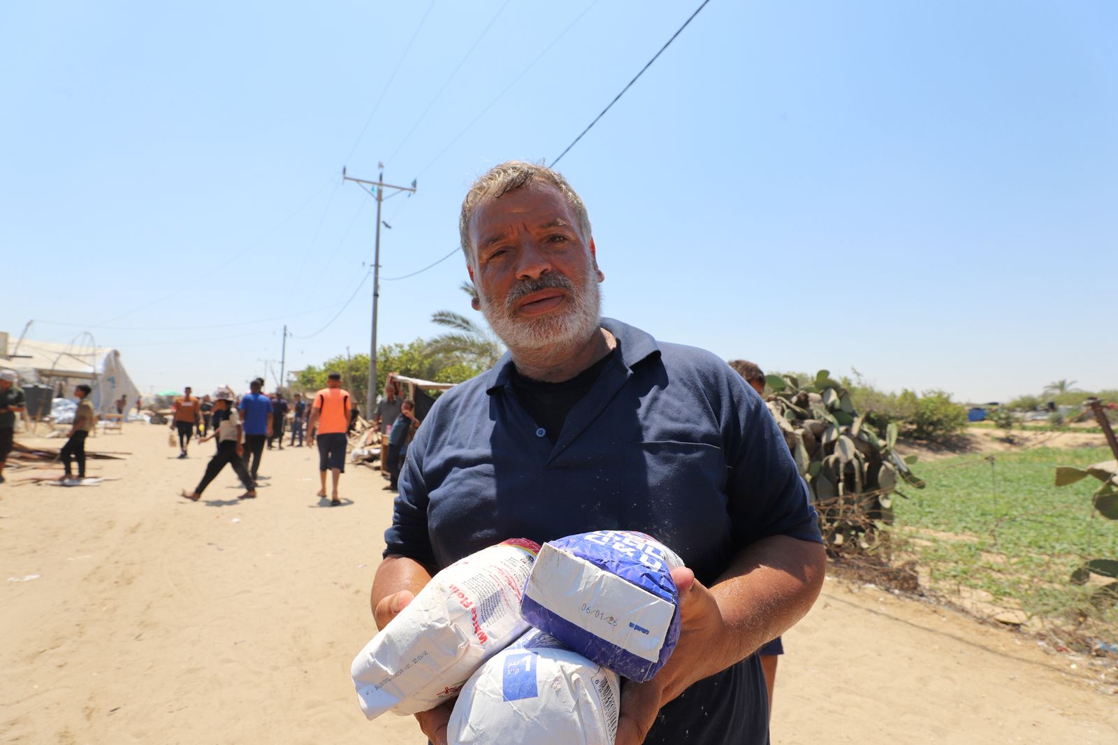 Fayez Abu Obeyd holds three white and blue packets of flour as he stands on an unsealed road.