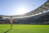 Western Bulldogs' Marcus Bontempelli kicks a ball in a sunlit stadium ahead of a match.