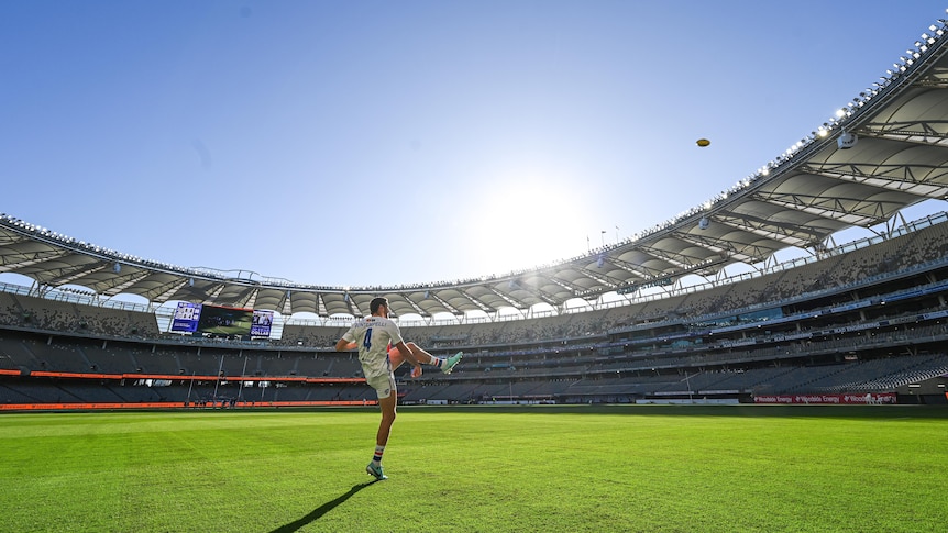 Western Bulldogs' Marcus Bontempelli kicks a ball in a sunlit stadium ahead of a match.