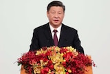 Xi Jingping in a suit standing at a lectern covered in flowers