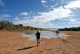 A man stands in front of the slowly creeping Gascoyne River with his back to the camera.