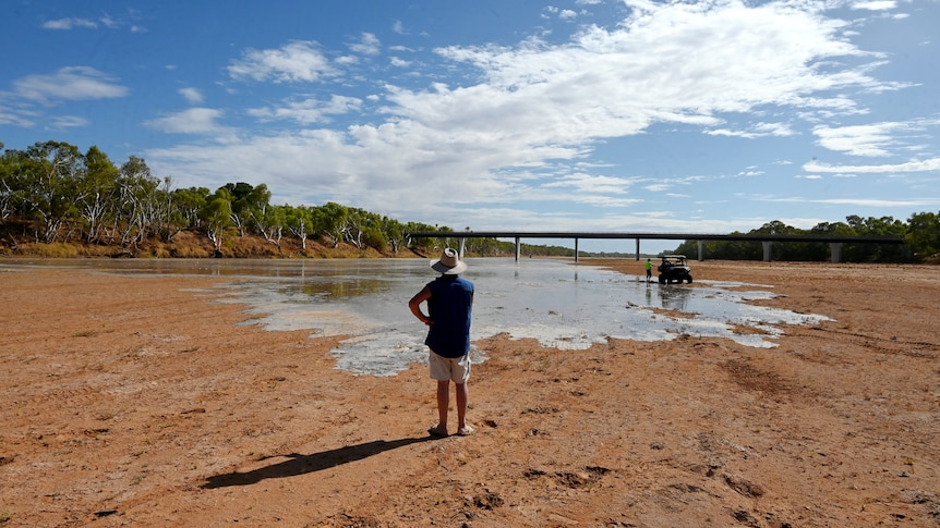 A man stands in front of the slowly creeping Gascoyne River with his back to the camera.