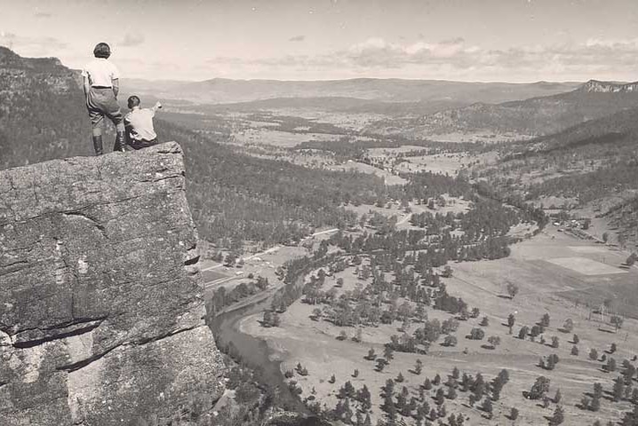 Two people stand on a rock overlooking a valley