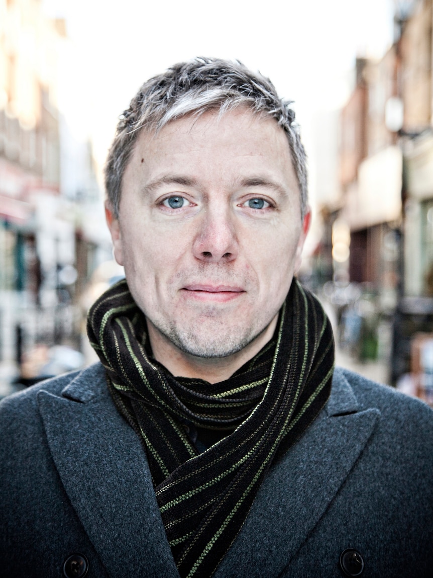 Portrait of a man with blue eyes and blond hair wearing a scarf on a UK street.