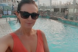A selfie of a woman in a swimsuit and sunglasses by a swimming pool on a cruise ship. 
