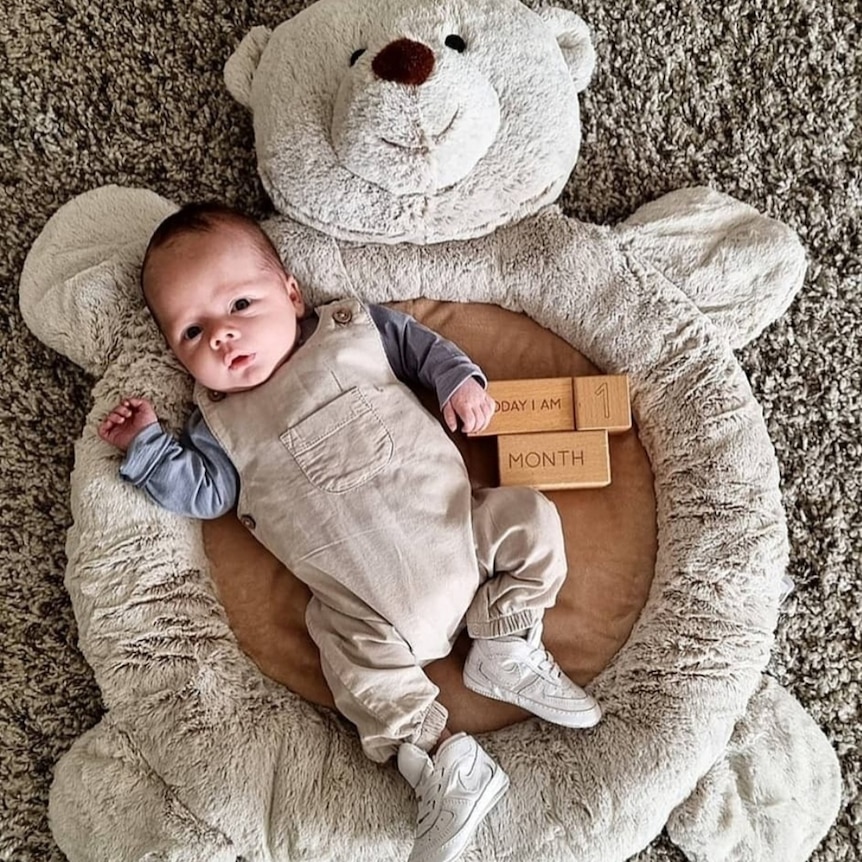 A bird's eye view of a baby boy lying on a round cushion.