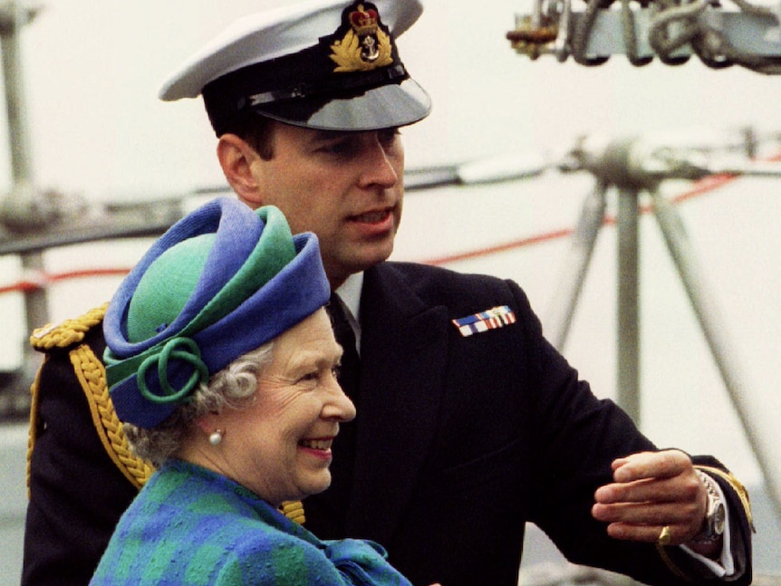 The Queen and Prince Andrew stand aboard a Royal Navy ship deck as the Royal directs the sovereign to another location.