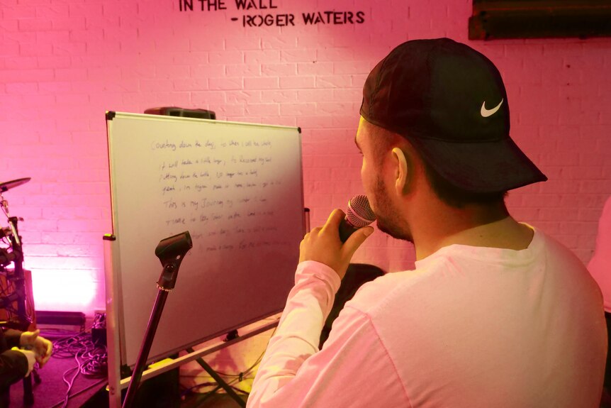 The back of a man with his hat on backwards singing into a mic in a studio
