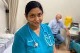  Dr Sonu Haikerwal stands in a treatment room at her practice, with a patient and nurse sitting behind her