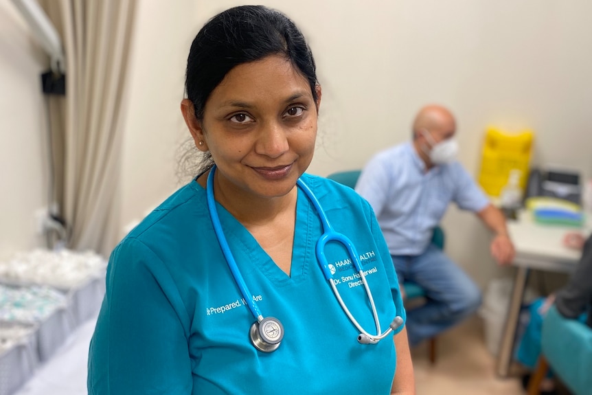  Dr Sonu Haikerwal stands in a treatment room at her practice, with a patient and nurse sitting behind her