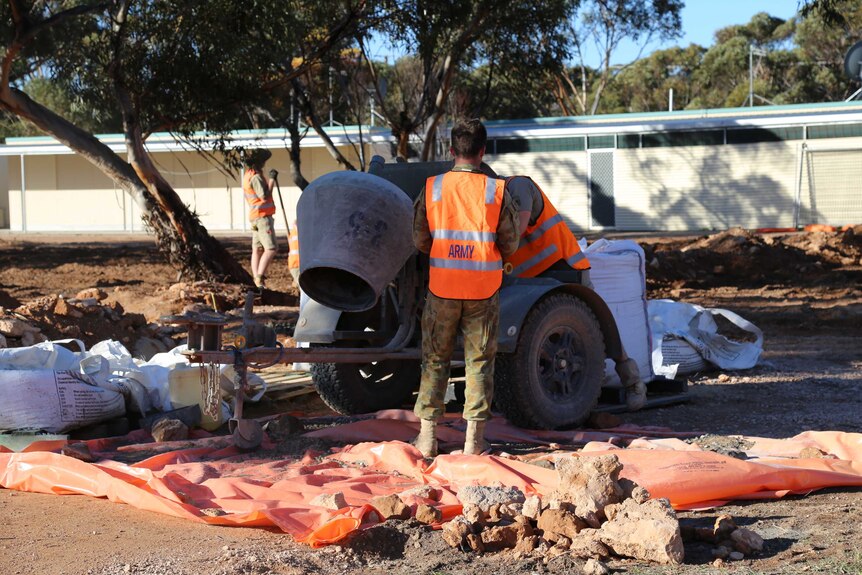 A man in a high vis vest saying "army" pours concrete.