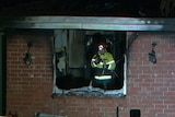 A firefighter through the broken window of a burnt out house