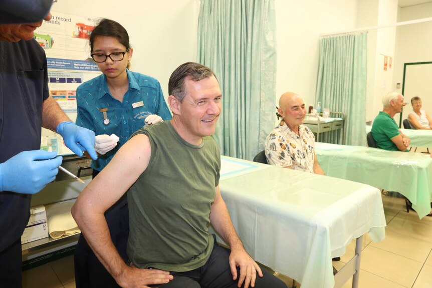 Chief Minister Michael Gunner sits in a health clinic, as two staff give him the AstraZeneca vaccination.