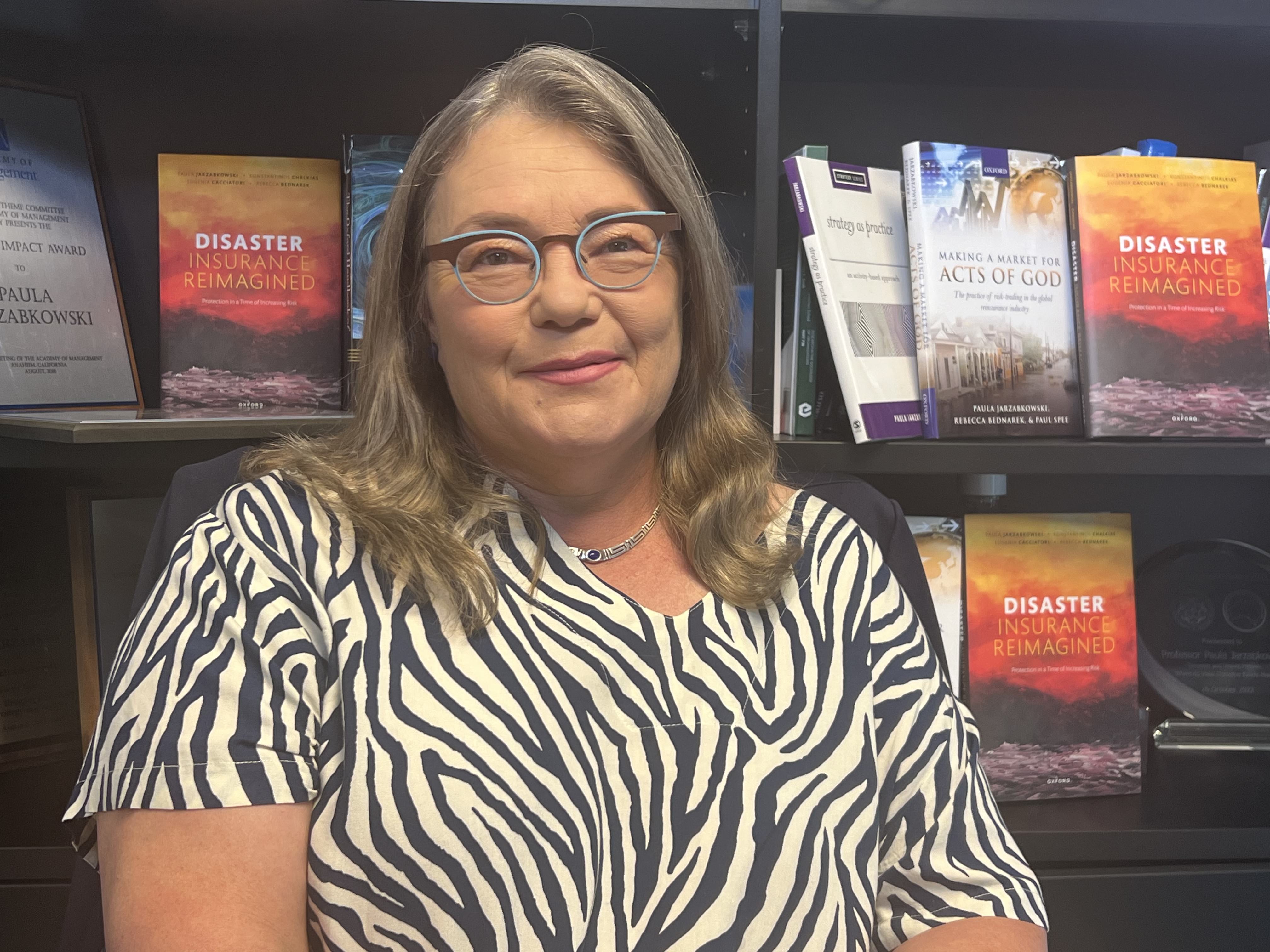 a university professor sitting in front of a bookshelf smiling at the camera
