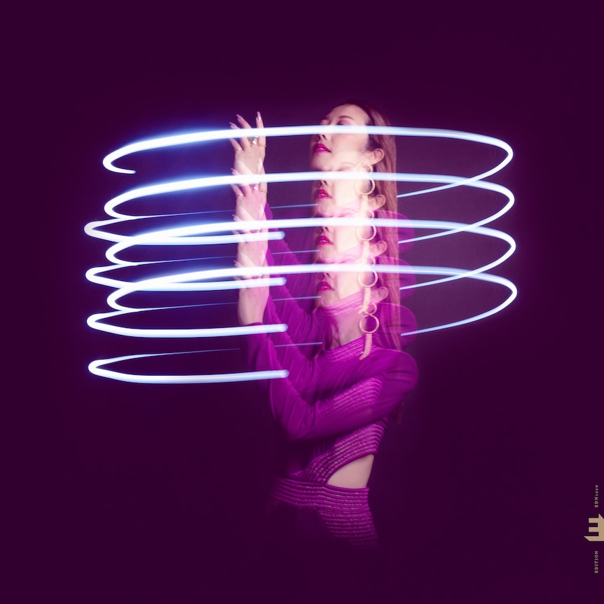 A multiple-exposure photo of Miho Hazama in purple, twirling a blue light