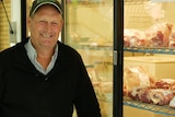 A man smiling standing in front of a cool room fridge of lamb
