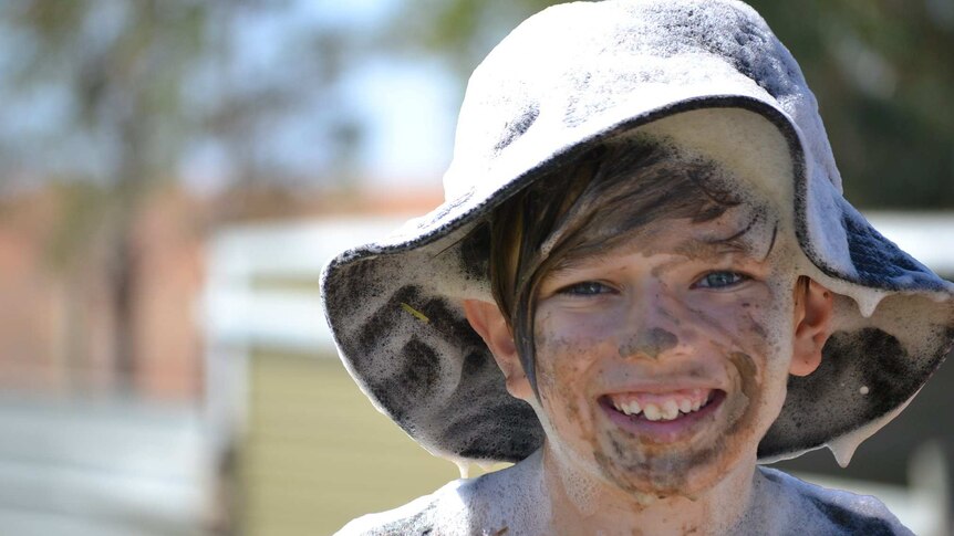 A young boy is smiling while covered in mud