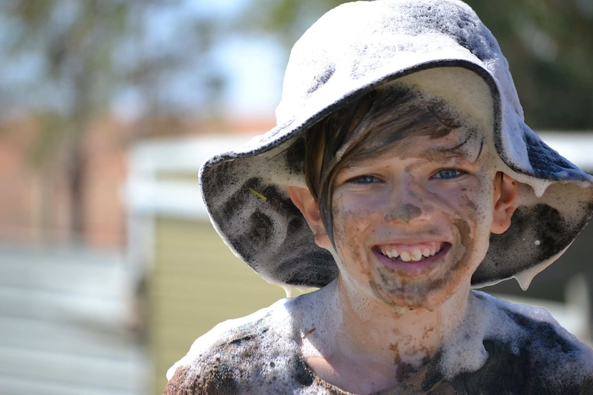 A young boy is smiling while covered in mud